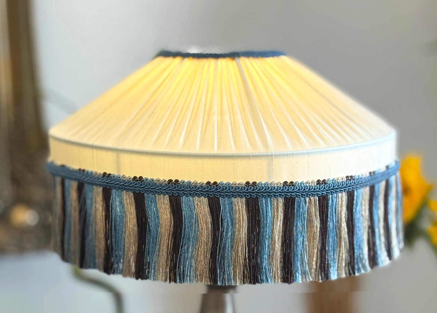 Close-up of a lampshade with pleated design and  blue striped trim.