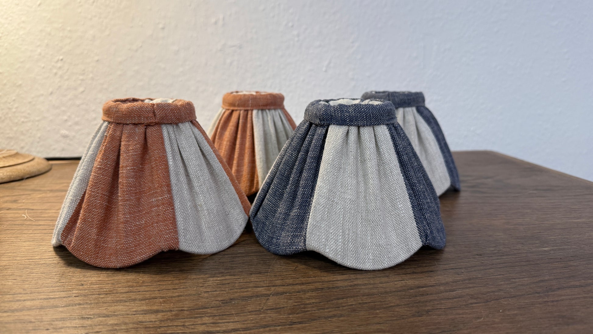 Four fabric clip-on lampshades with different color combinations on a wooden surface.