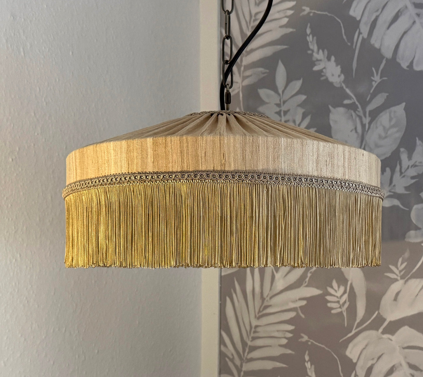 Pendant light with gold fringe shade against a floral wallpaper background